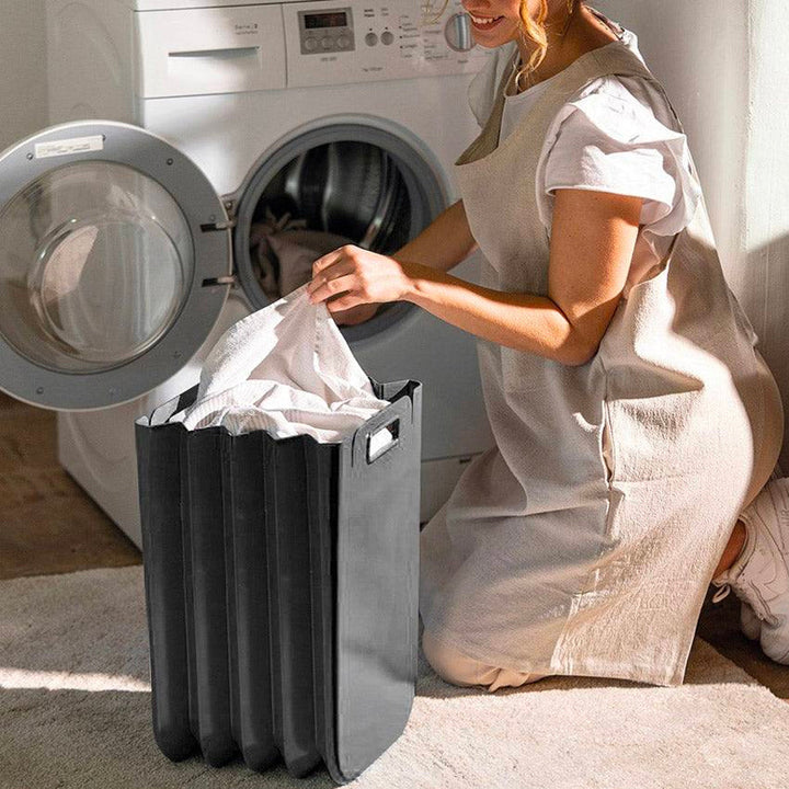 Contenedor multipropósito Eco Packly negro de Guzzini con ropa junto a una lavadora